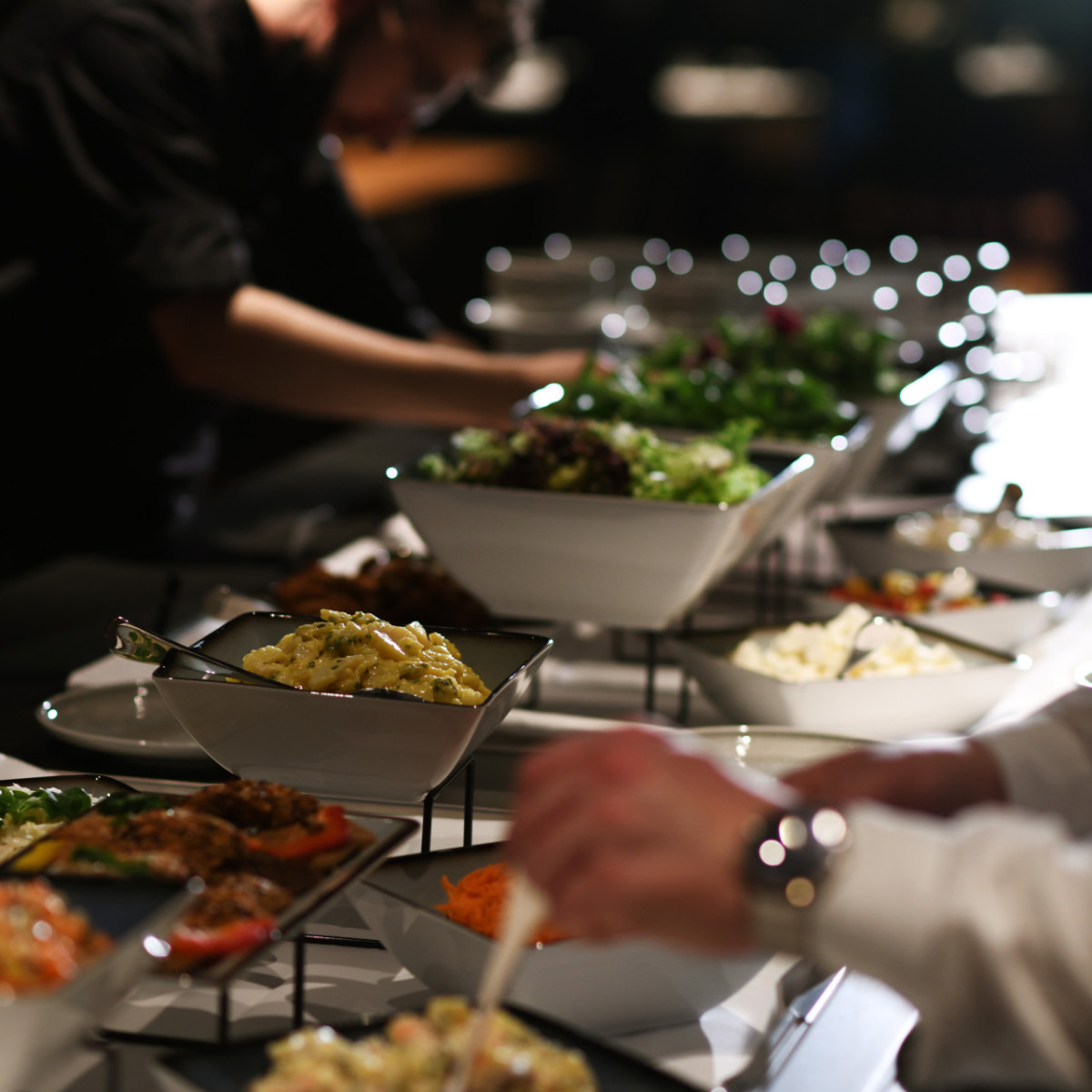 emser thermenhotel restaurant buffet v2 Ein Buffet mit verschiedenen Speisen in eleganten Schalen. Zwei Personen bedienen sich. Eine Vielfalt an Salaten, Beilagen und Hauptgerichten ist deutlich zu erkennen. Hintergrund ist weichgezeichnet.