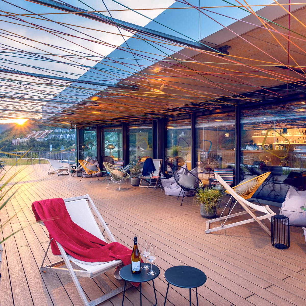 emser thermenhotel rooftop bar skylounge dachterrasse sonnenuntergang Gemütliche Terrasse mit modernem Design, geschmückt mit bunten Fäden. Sonnenuntergang im Hintergrund, Loungemöbel, Pflanzen und Getränke auf kleinen Tischen laden zum Entspannen ein.